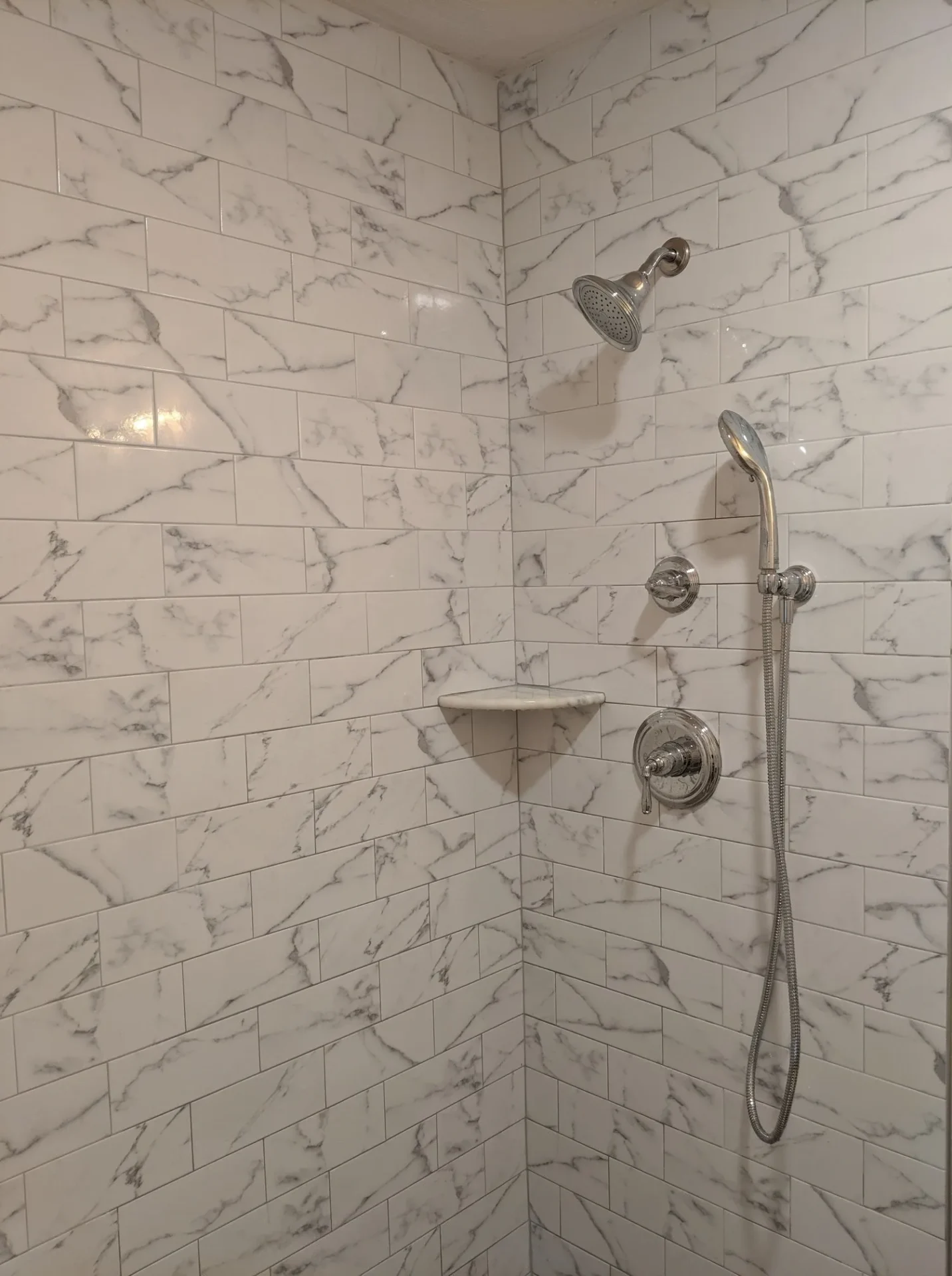 A shower with marble walls and white tile.